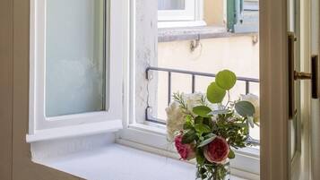 Une pièce avec une fenêtre, une porte et un petit banc près de la fenêtre, sur lequel est posé un vase de fleurs.
