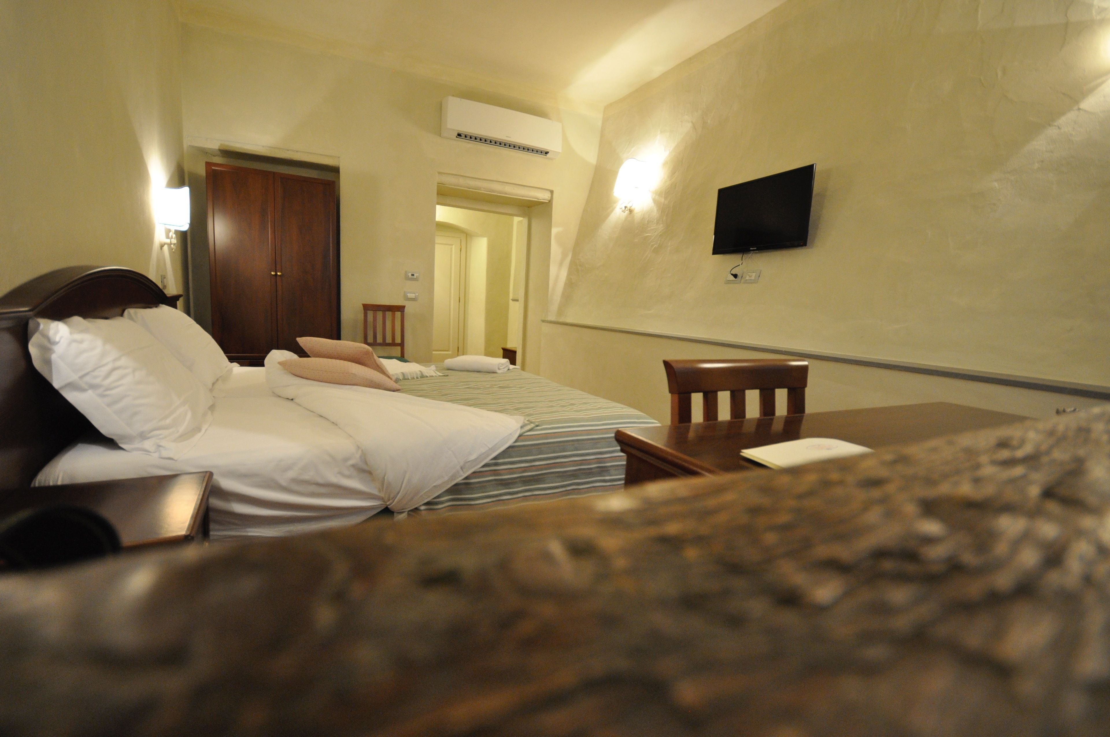 A hotel room with a bed, a desk, a chair, a television, and an air conditioning unit.