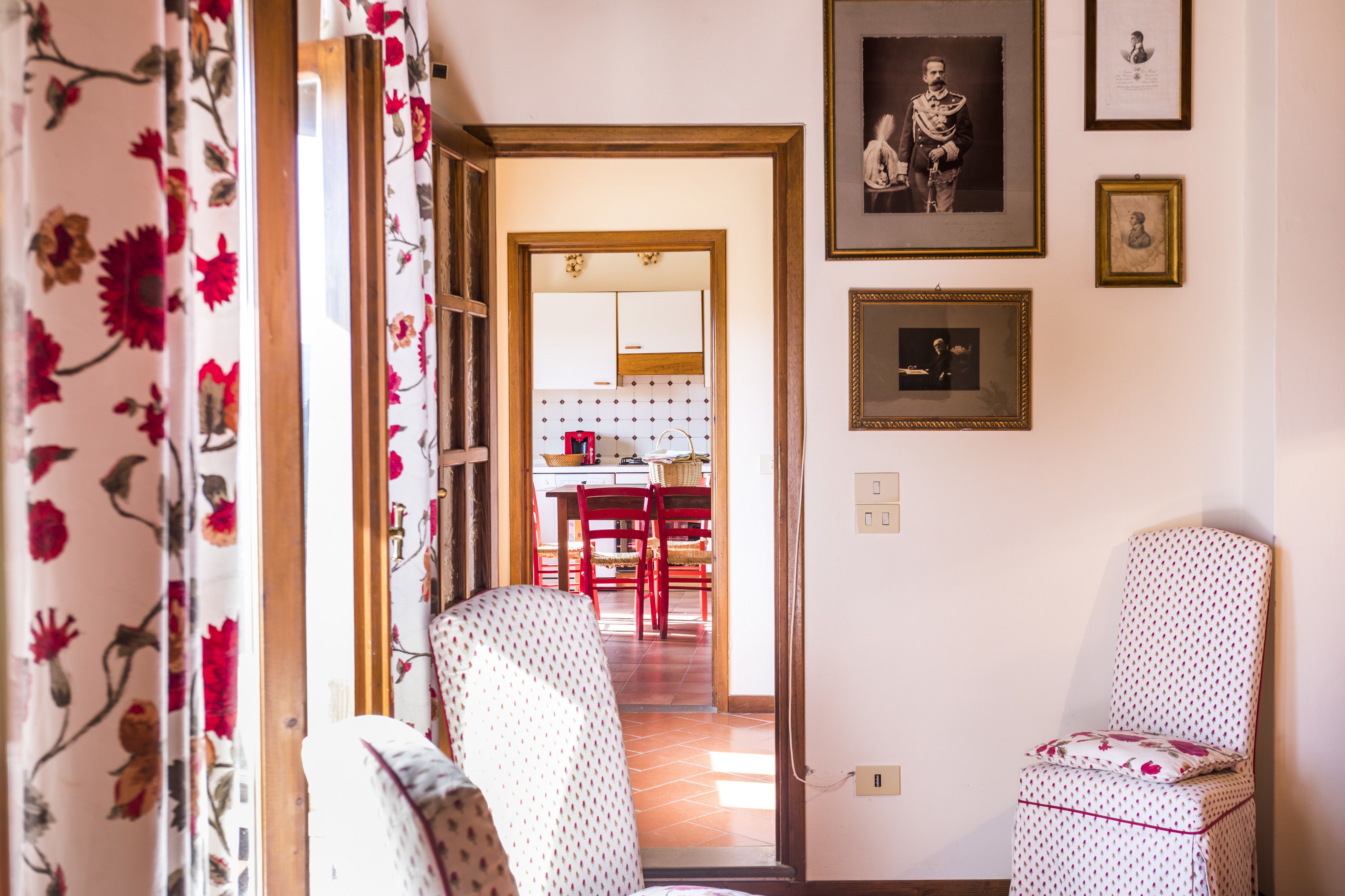 Una habitación con dos sillas estampadas, una zona de comedor con sillas rojas y cuadros en la pared.