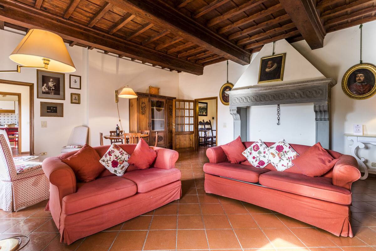 A cozy living room with two red sofas, a wooden ceiling, and a fireplace.