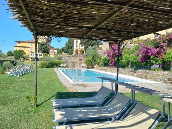 A pool area with lounge chairs, a pergola, and a stone wall with flowering plants. - Fattoria di Maiano (Fiesole)