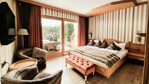 Un dormitorio con una cama grande, una zona de estar con un banco, un televisor y vistas al exterior.