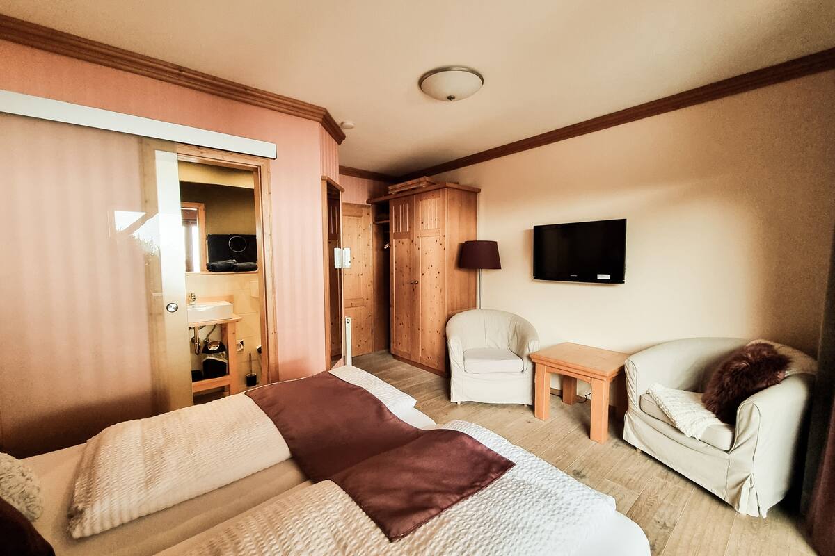 A hotel room with a bed, two chairs, a small table, a TV, and a wardrobe.