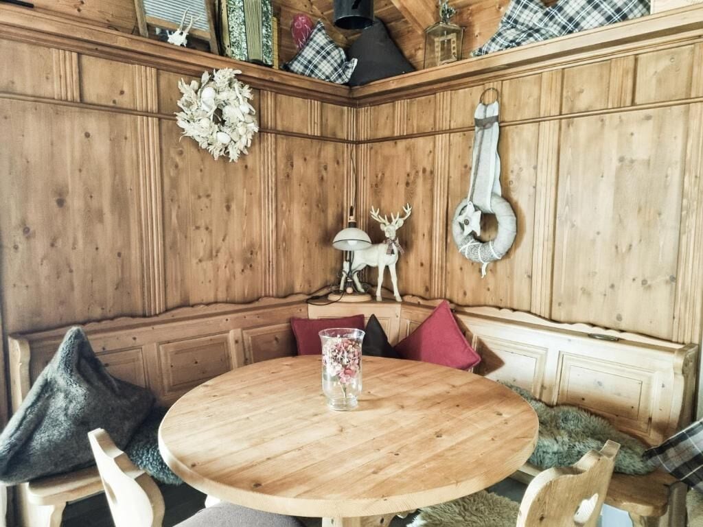 Un interior de madera con una mesa redonda, un adorno de guirnalda y una lámpara de pared.