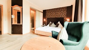 Una habitación de hotel con una cama, un sillón verde, una mesa redonda de madera, un espejo y una zona de ducha.