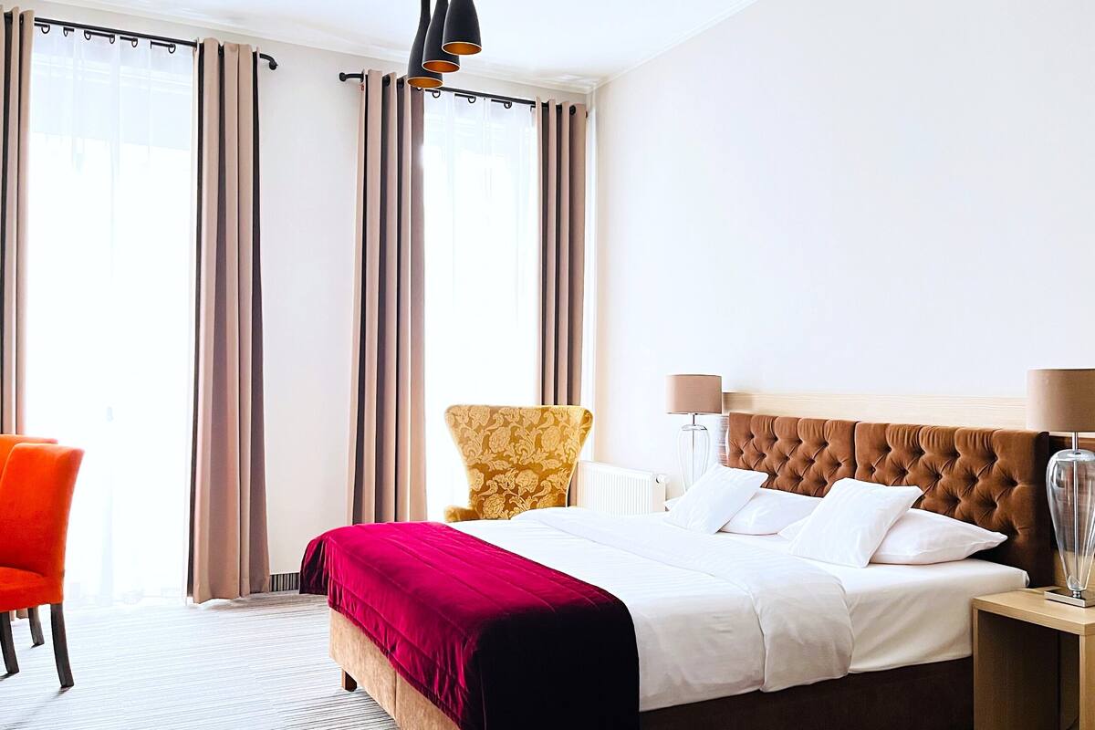 A hotel room with a large bed, a chair, a lamp, and a window with curtains.