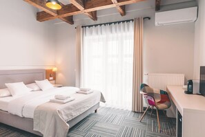 Habitación de hotel con cama, escritorio, silla, radiador y ventana con cortinas.
