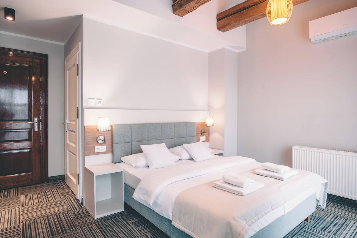 A hotel room with a bed, bedside tables, a nightstand, a wooden door, and a radiator.