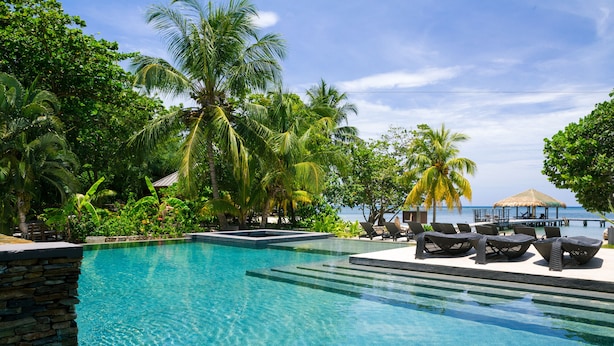 A clear blue pool with lounge chairs and palm trees. - Xbalanque (Roatan)