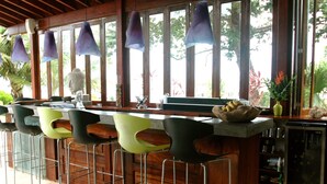 A bar area with a wooden counter, bar stools, and pendant lighting. - Xbalanque (Roatan)