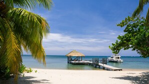 A beach with a thatched-roof hut and a dock extending into the water. - Xbalanque (Roatan)