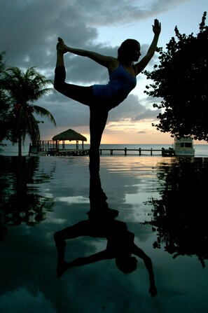 A person performing a yoga pose on a reflective surface with a sunset and a pier in the background.