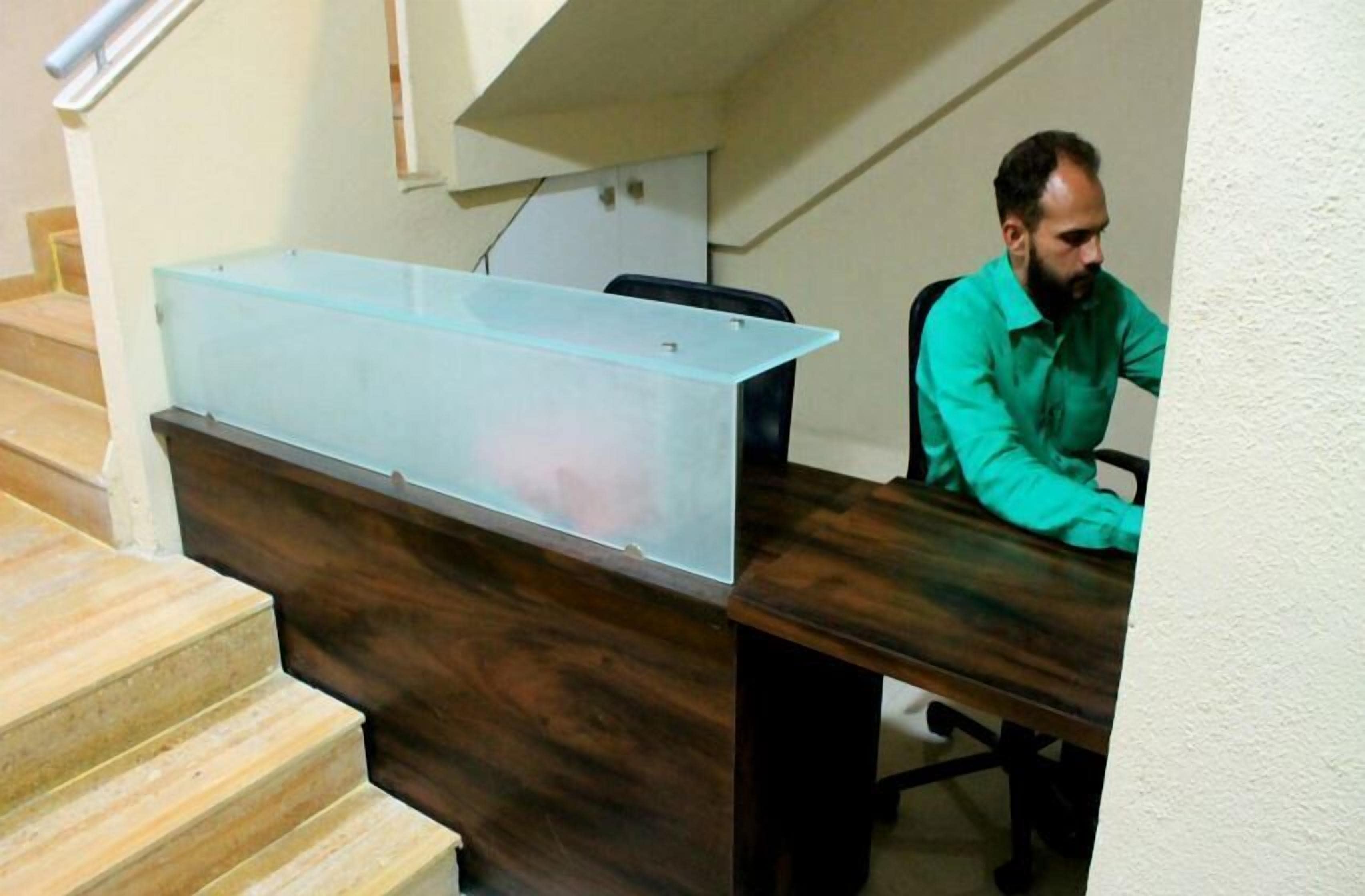 Una persona sentada en un escritorio con un contenedor de plástico transparente grande sobre él.