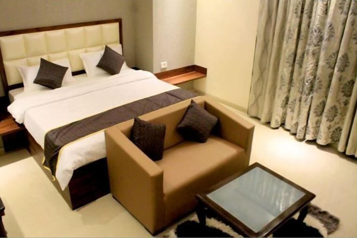 A hotel room with a bed, a sofa, a coffee table, and a curtain.