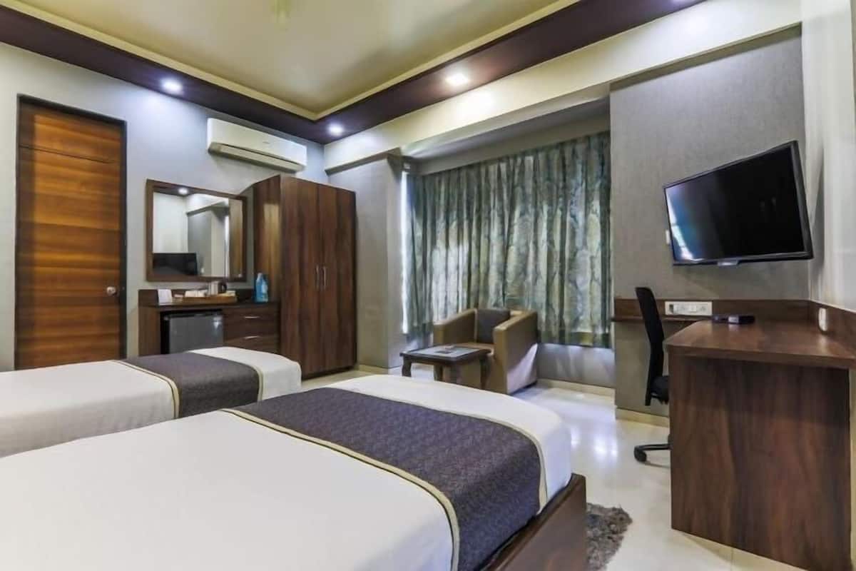 Habitación de hotel con dos camas, un escritorio, una silla, un televisor y un ventanal con cortinas.