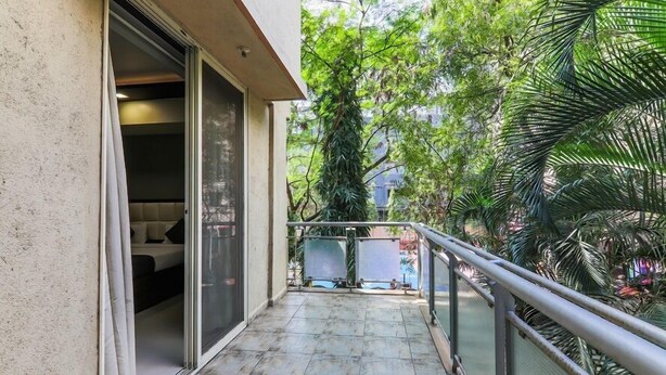 Un balcon donnant sur un espace verdoyant et l’entrée d’un immeuble.
