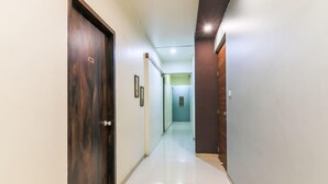 Un couloir avec une porte en bois sur la gauche, un tableau encadré au mur et un plancher de couleur claire.