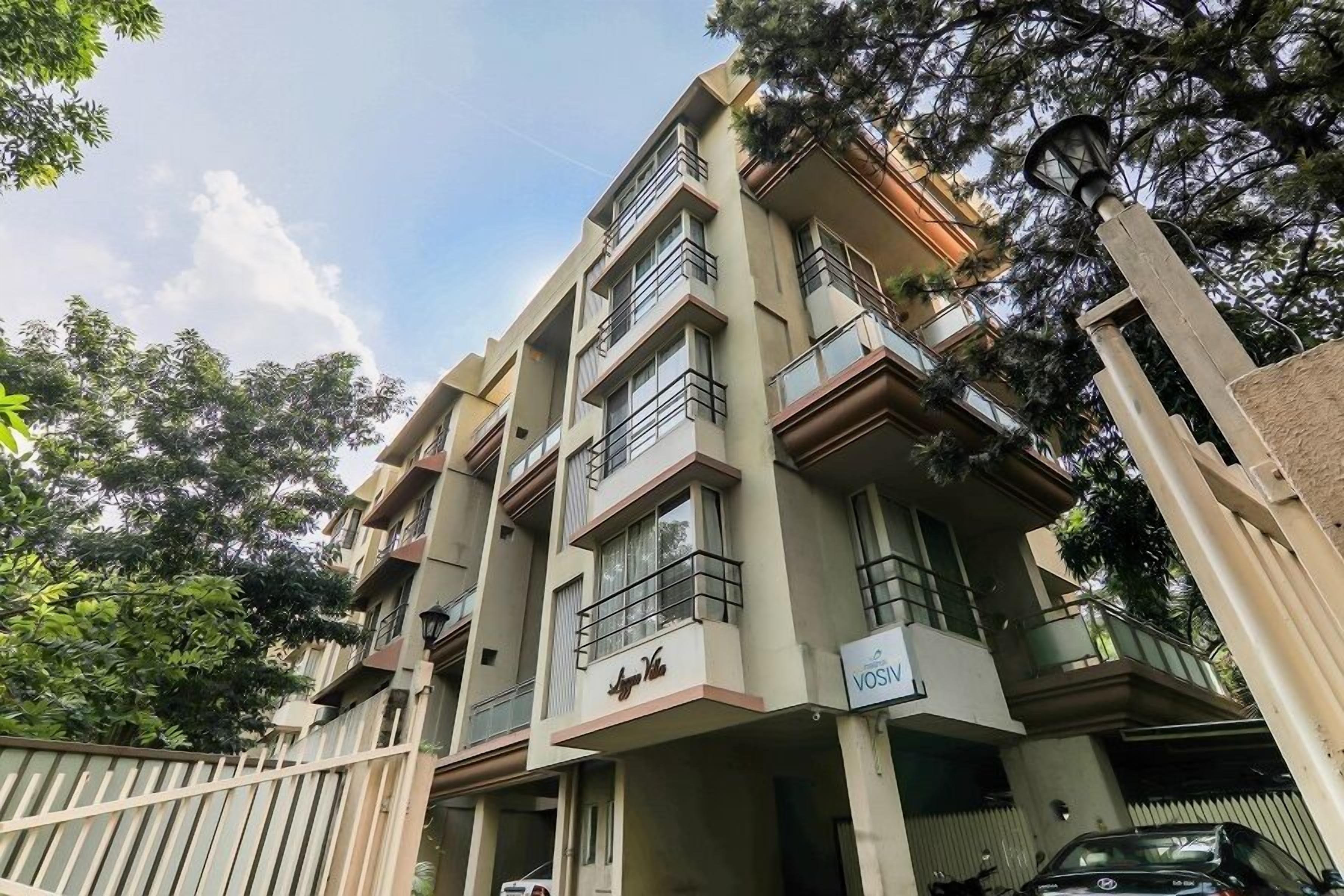 A multi-story residential building with balconies, a gated entrance, and a sign indicating "VOSIN".