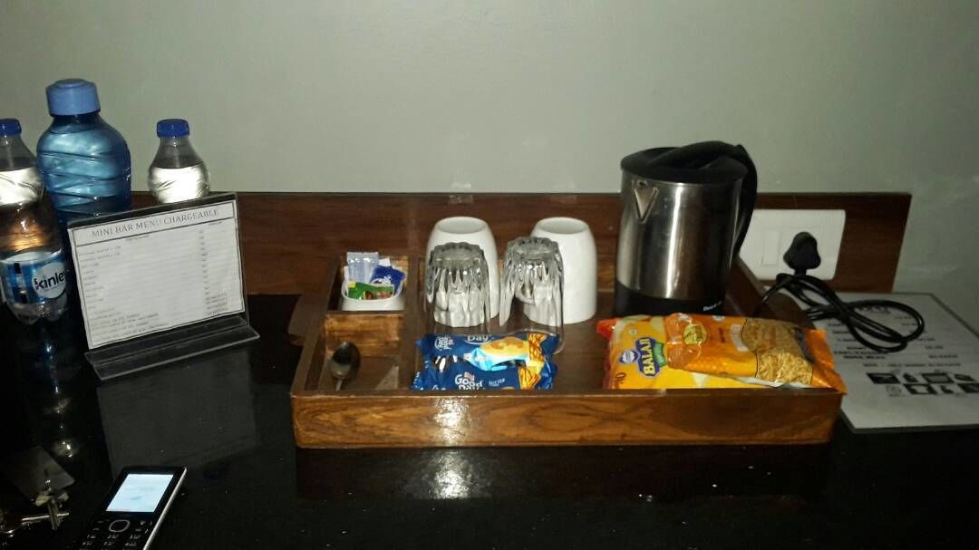 A hotel room's reception area with a wooden tray holding snacks, a kettle, and a mobile phone.