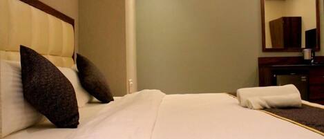 A hotel room with a bed, pillows, a bedside table, a mirror, and a small cabinet.