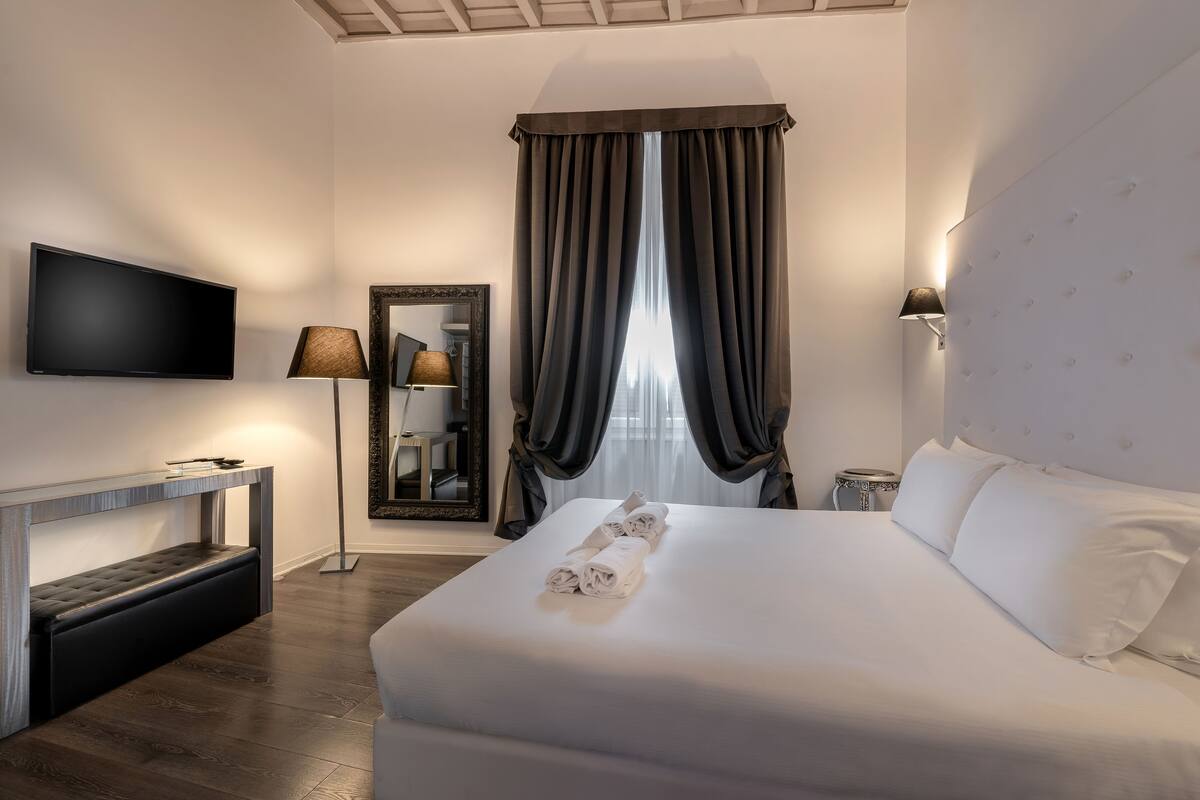 A hotel room with a large bed, a flat-screen TV, a bedside table, a lamp, and a mirror.