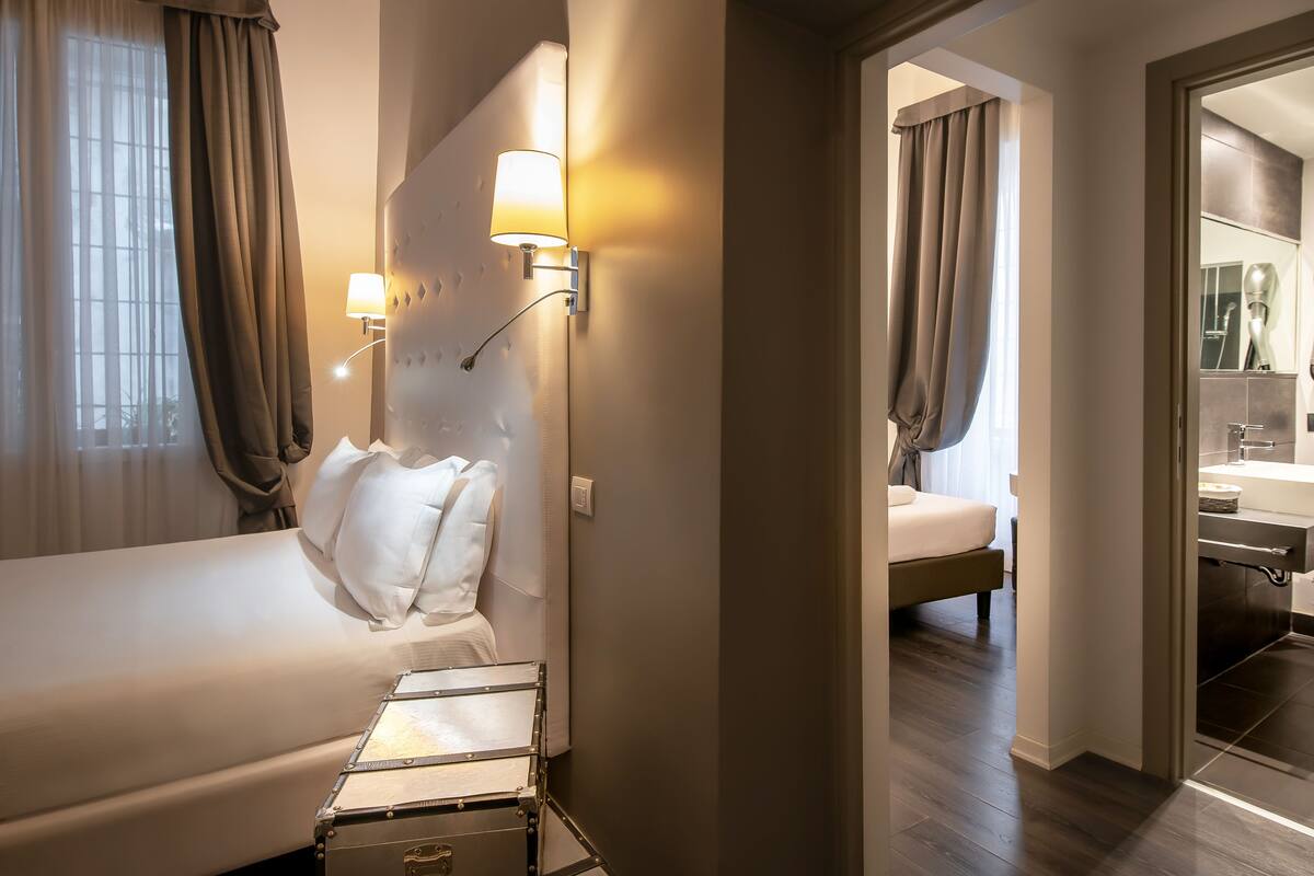 A hotel room with a bed, a bedside lamp, a suitcase, and a bathroom with a mirror and sink.