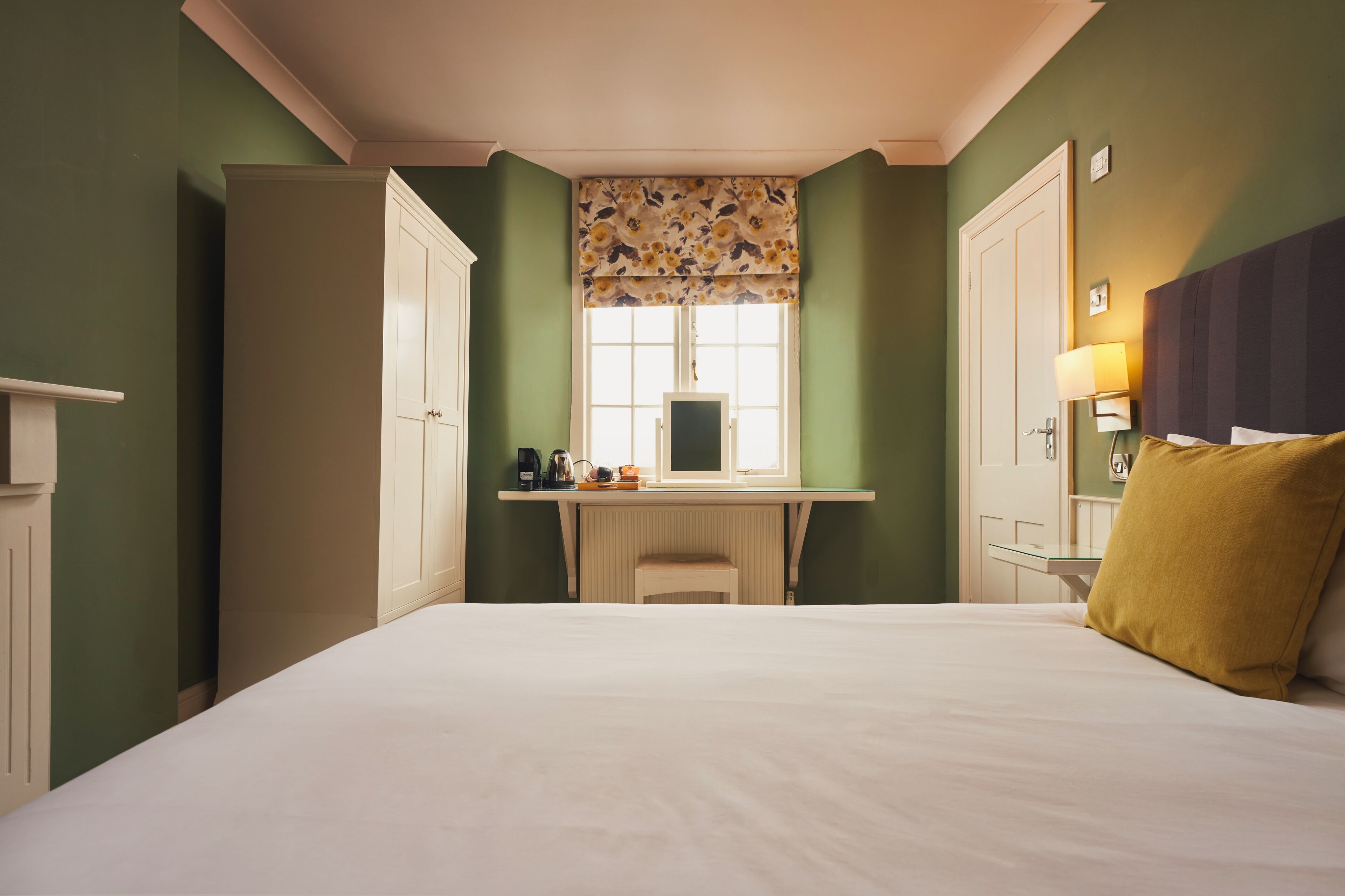 Una habitación de hotel con cama, escritorio y ventana con cortina decorada con motivos florales.