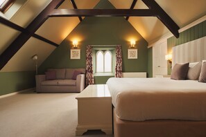 A cozy attic bedroom with a sloped ceiling, a bed, a sofa, and two wall-mounted lamps. - Rose & Crown (Plymouth)