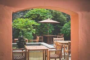 An outdoor patio area with wooden tables and chairs, a stone fountain, and lush greenery. - Rose & Crown (Plymouth)