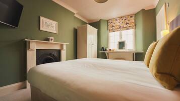 A bedroom with a bed, a fireplace, a desk, and a window with floral curtains.