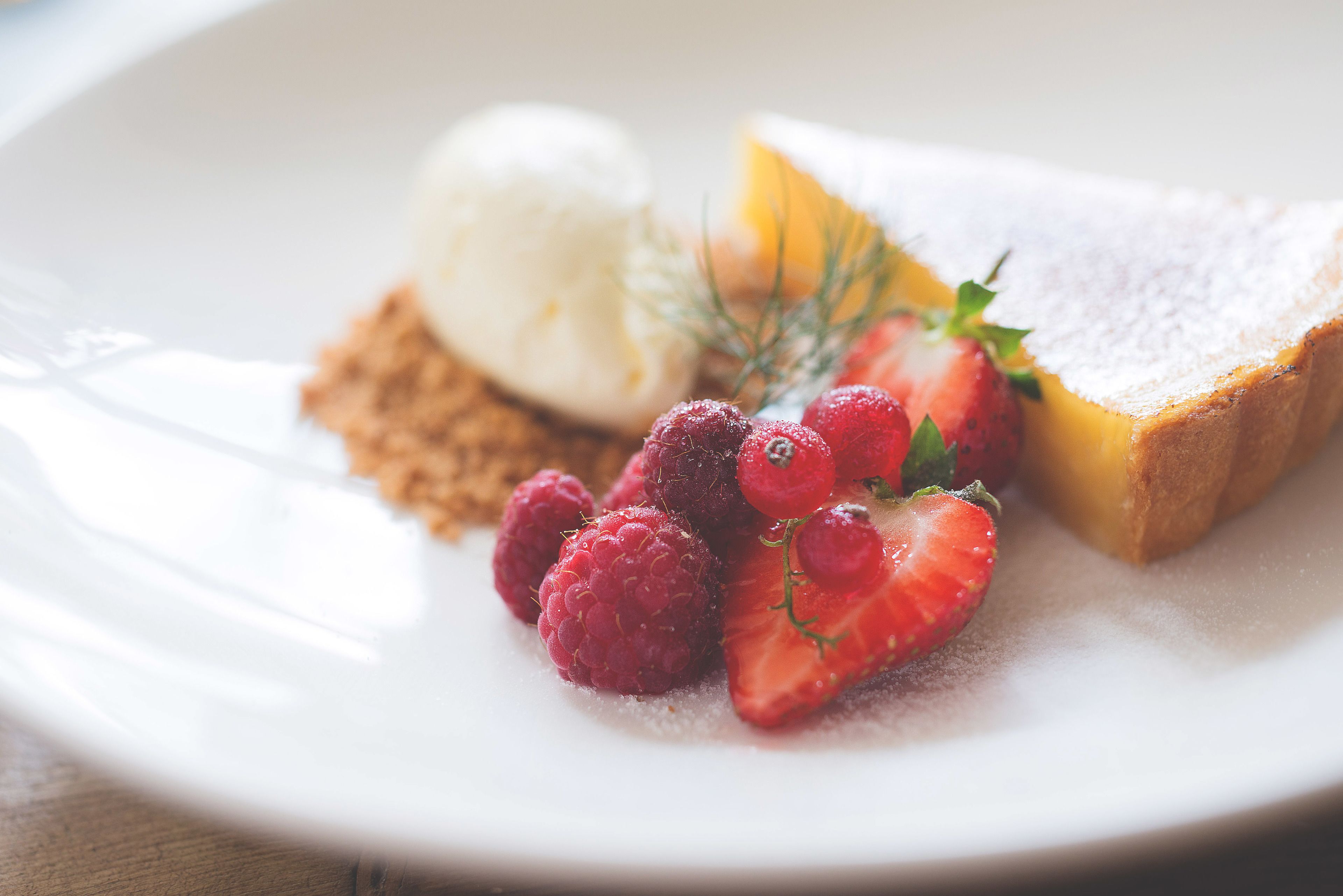 Un plato de postre con una rebanada de pastel, una bola de helado y frutos rojos frescos.