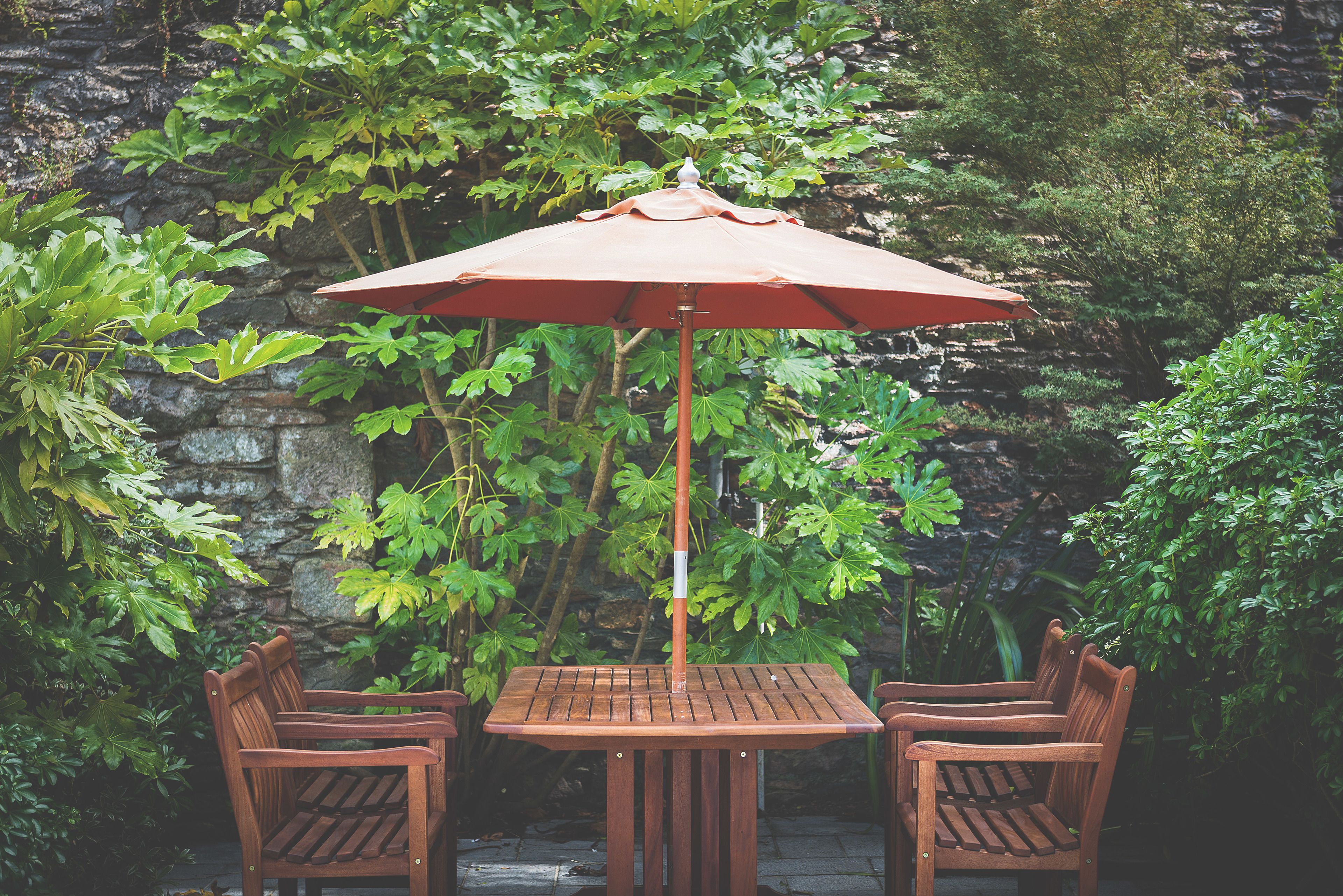 Una mesa de madera y dos sillas con un paraguas rojo en un jardín.