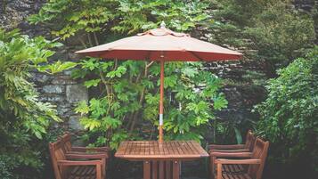 Una mesa de madera y dos sillas con un paraguas rojo en un jardín.