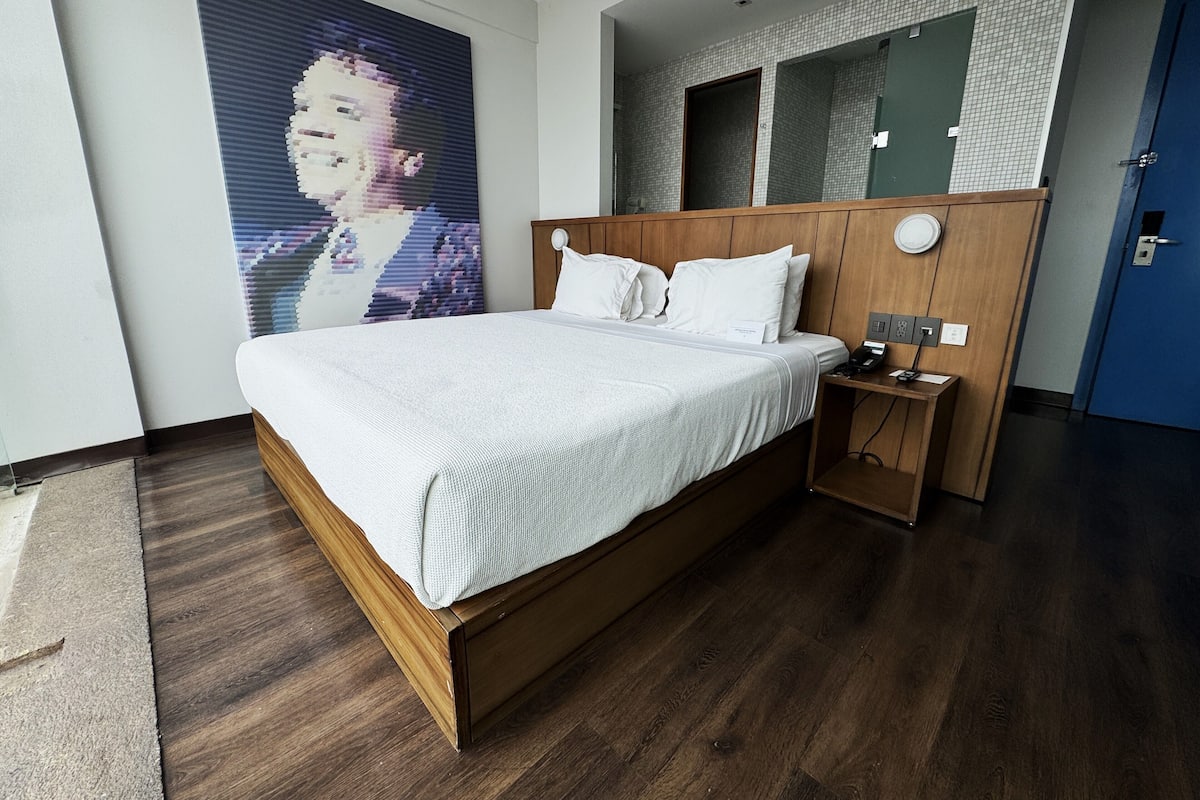 A modern hotel room with a large bed, wooden headboard, and a bedside table with a phone and charger.