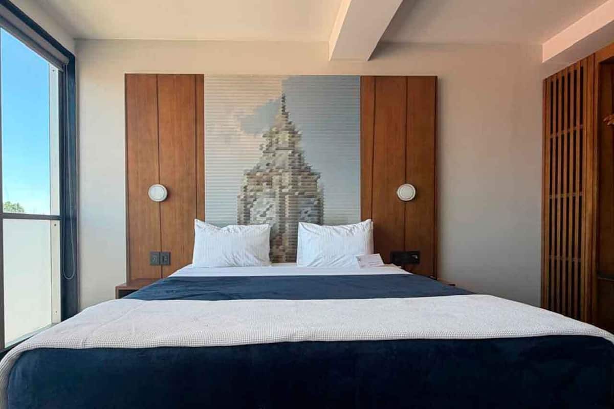 A bedroom with a large bed, wooden headboard, two wall-mounted lights, and a large window.