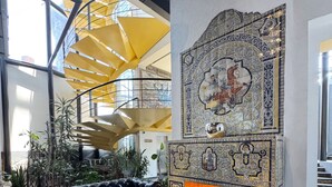 Un interior moderno con un sofá de cuero negro, una chimenea con detalles de azulejos intrincados y una escalera de caracol con toques de color amarillo.