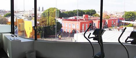 Un gimnasio con equipo de ejercicio y un amplio ventanal con vistas a la ciudad.