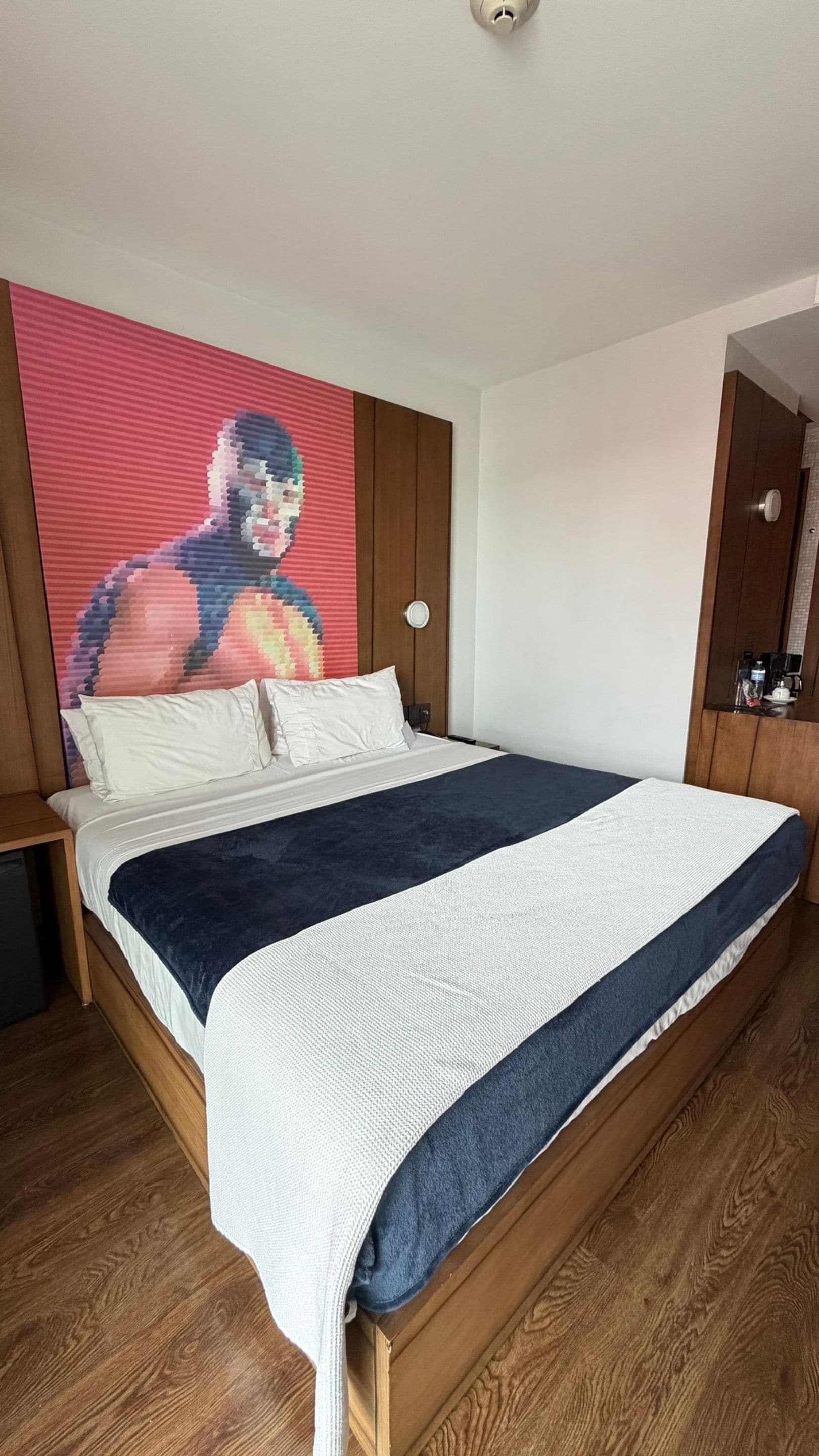 Un dormitorio con cama, cabecera de madera, una obra de arte grande en la pared y suelo de madera.
