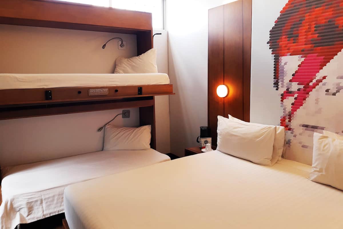 A hotel room with a bunk bed, a single bed, and a wall-mounted light fixture.