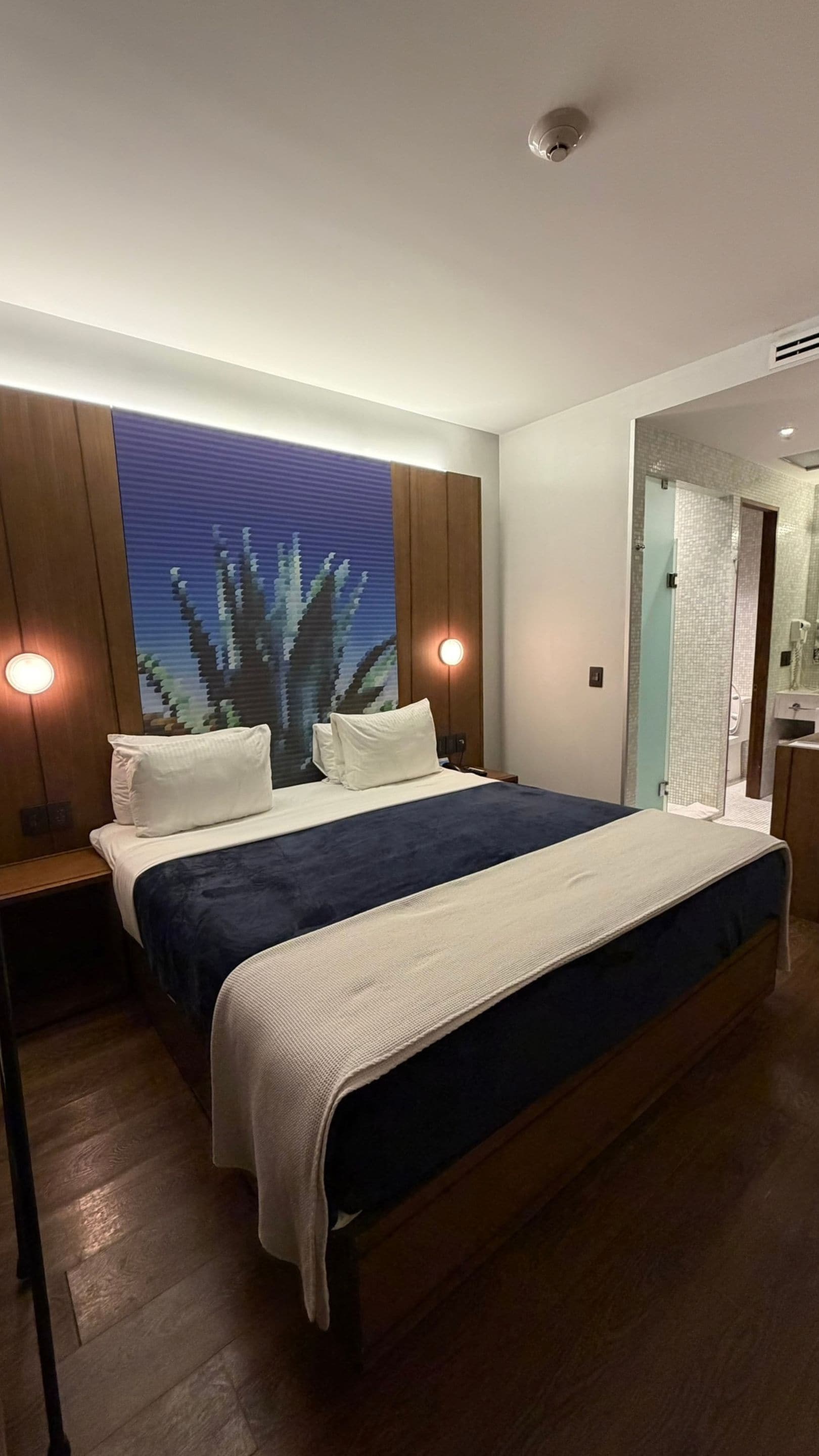 Una moderna camera d'hotel con un letto grande, una testiera in legno e un'opera d'arte appesa al muro.