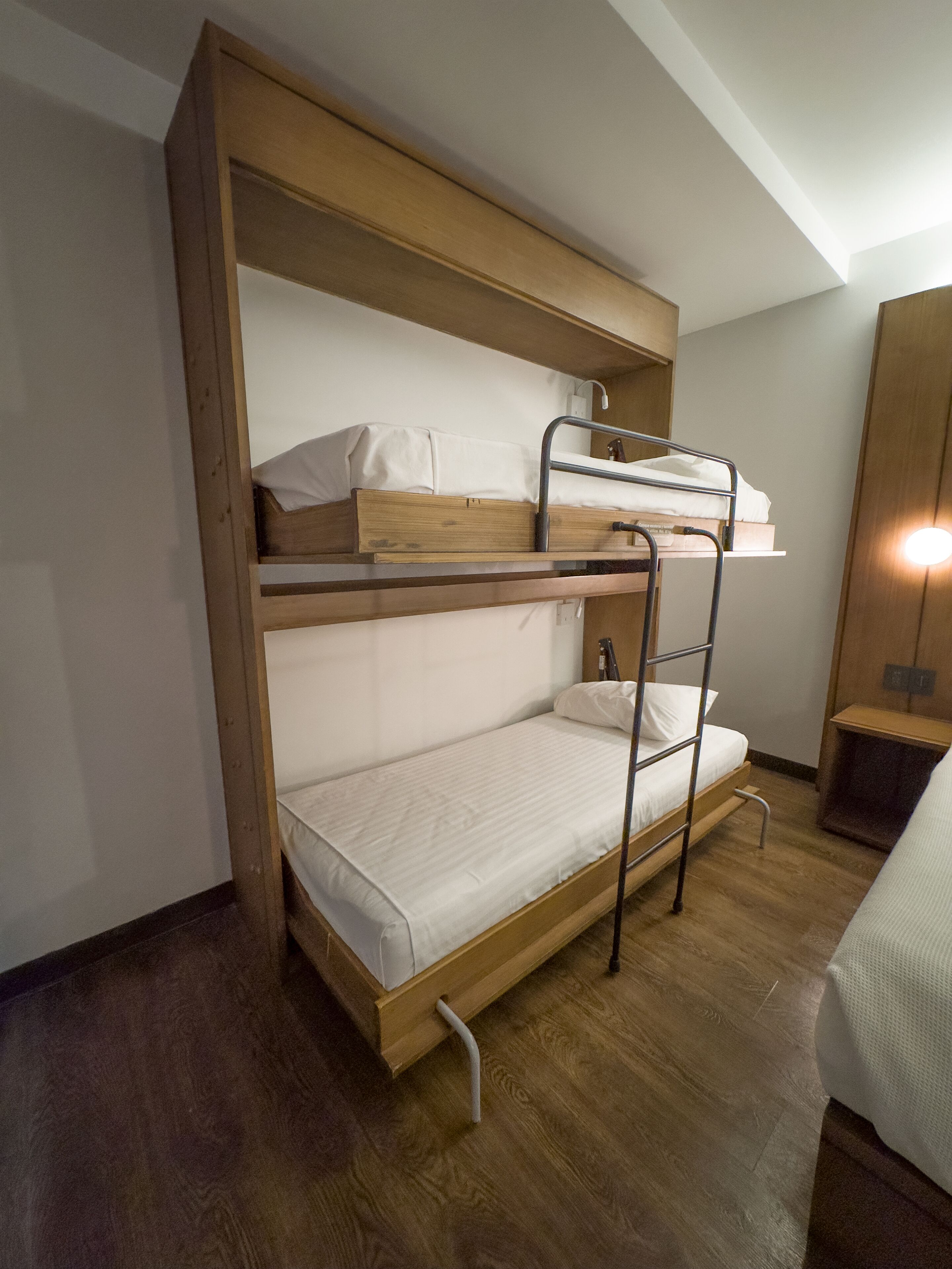 Una cama litera con estructura de madera, un escritorio abatible y una mesita de noche.