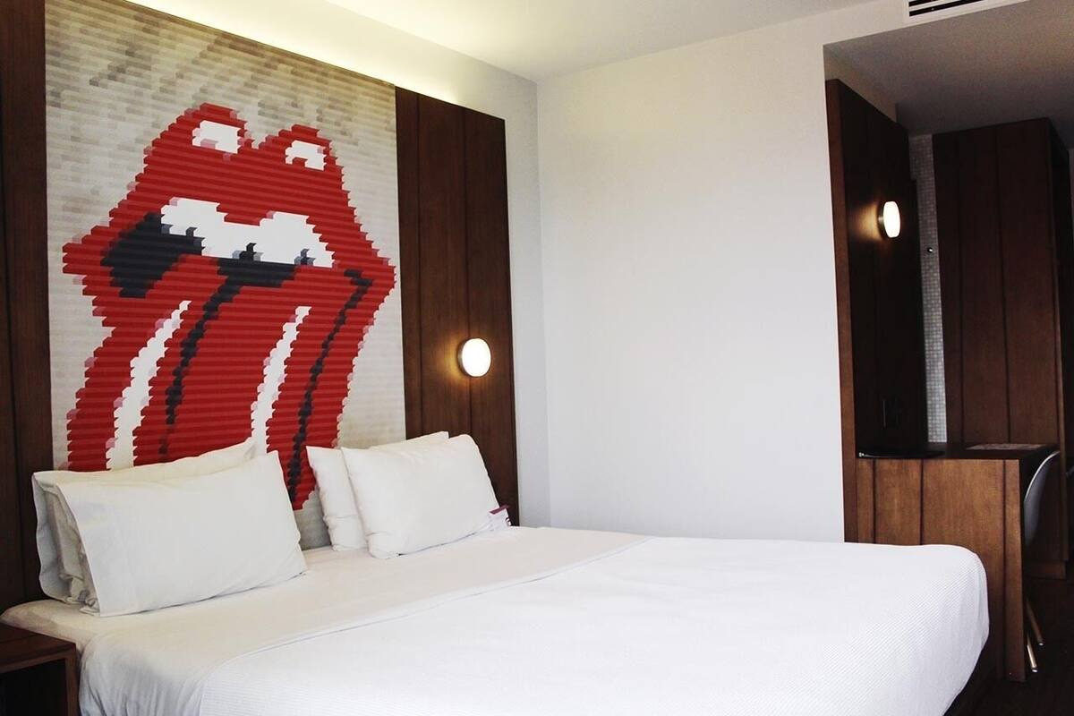 A hotel room with a large bed, white bedding, a wall art of lips, and a TV on a wooden cabinet.