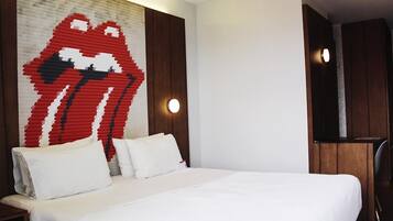 Habitación de hotel con una cama grande, ropa de cama blanca, un cuadro de labios en la pared y un televisor sobre un mueble de madera.
