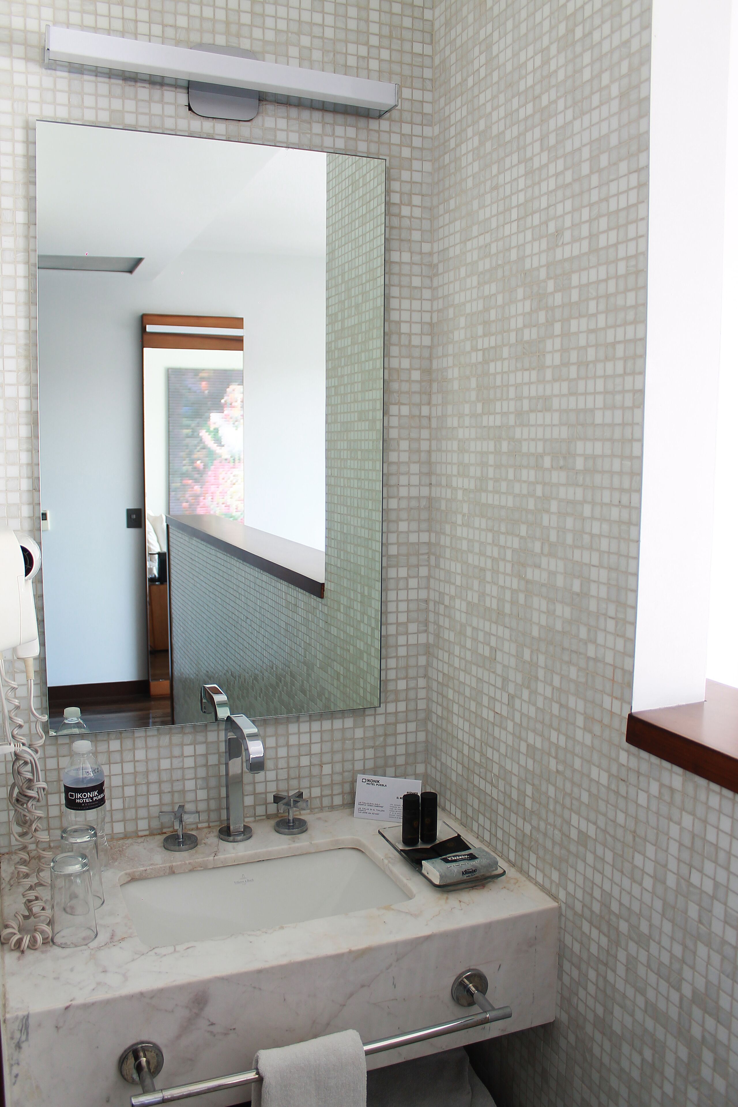 Un baño con un espejo grande, un lavabo y un perchero para toallas.