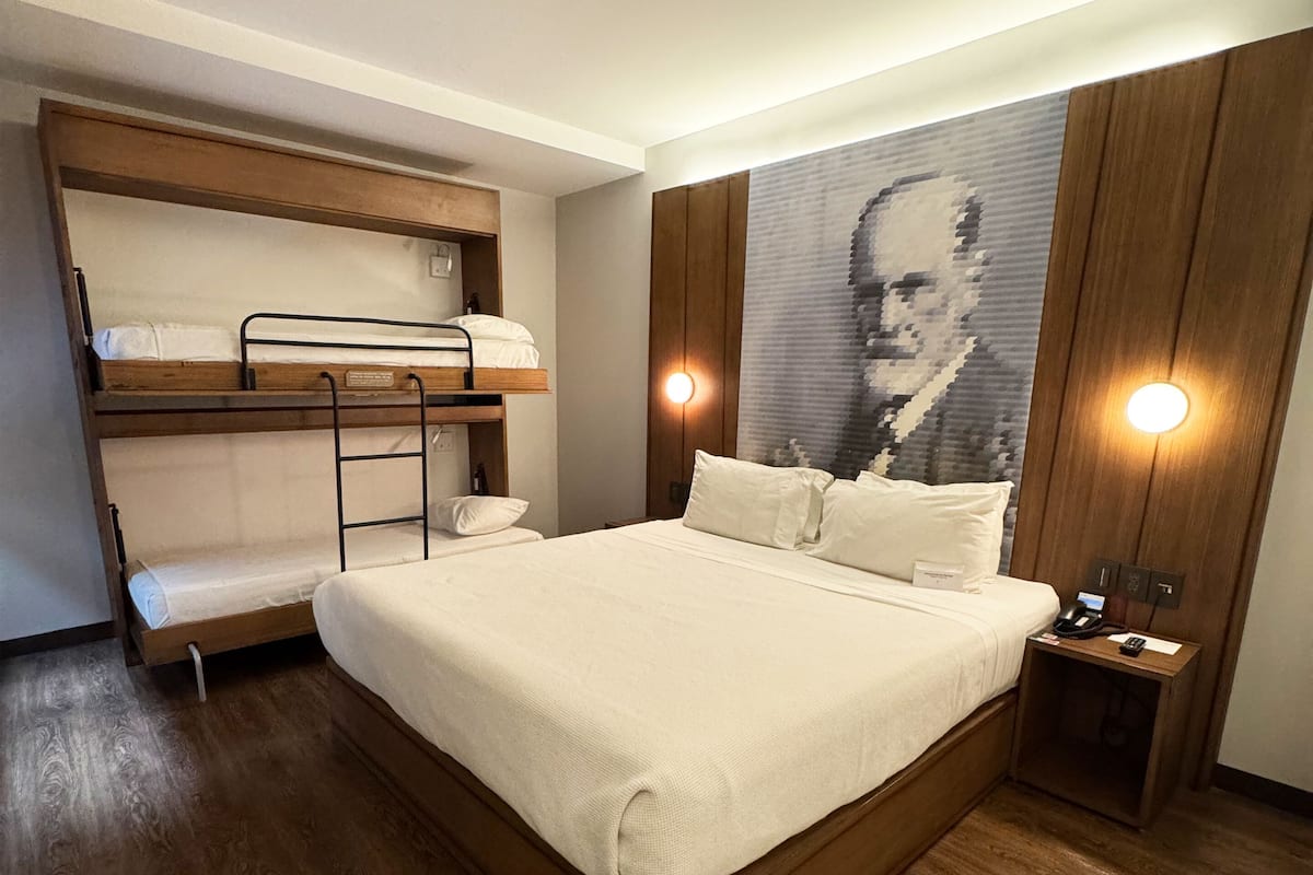 A bedroom with a large bed, a bunk bed, wooden flooring, a wall-mounted light, and a ceiling light.