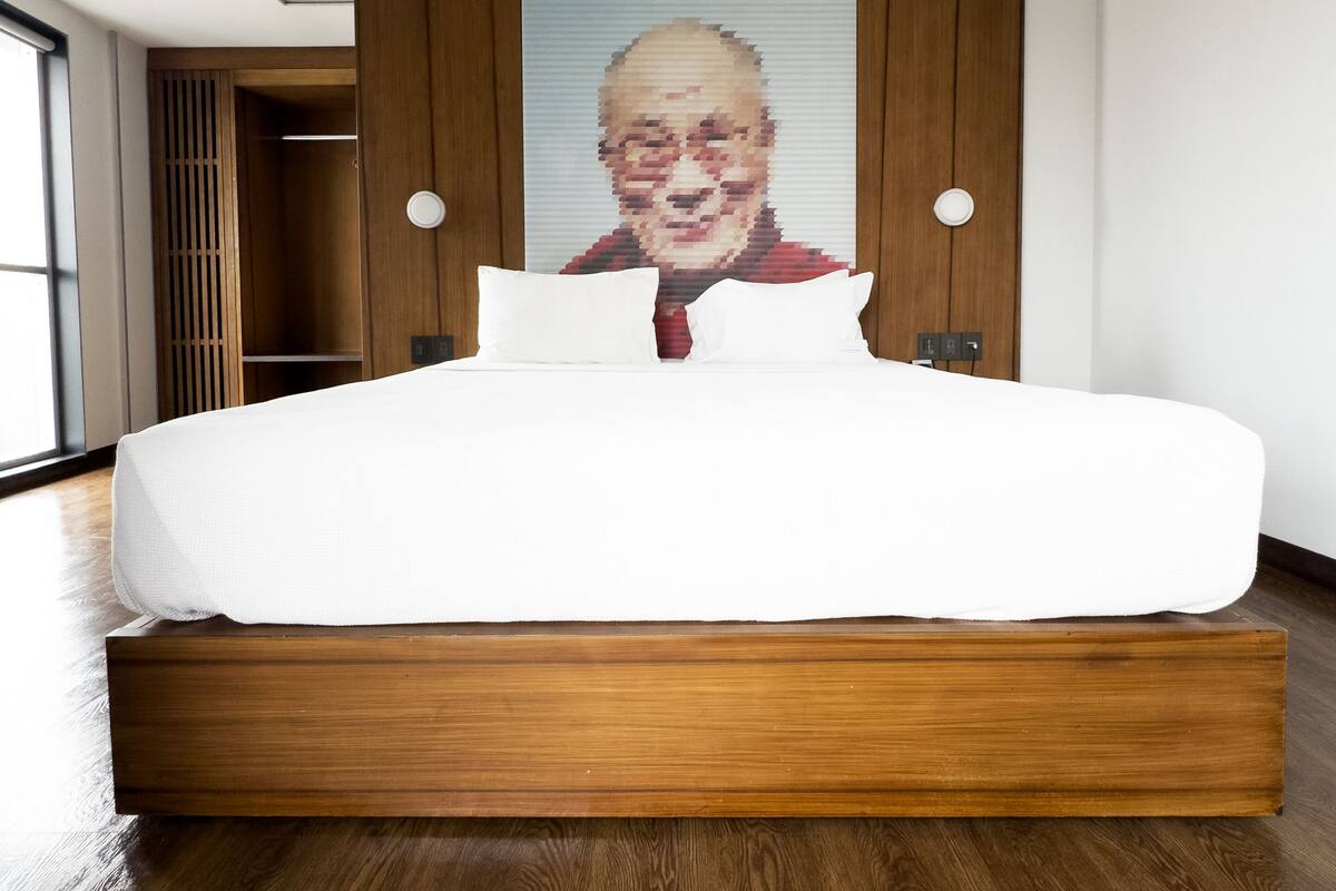 A modern hotel room with a large bed, wooden headboard, and a large portrait on the wall.