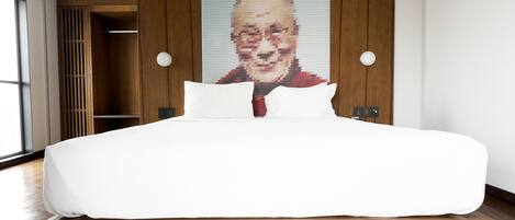 A modern hotel room with a large bed, wooden headboard, and a large portrait on the wall.