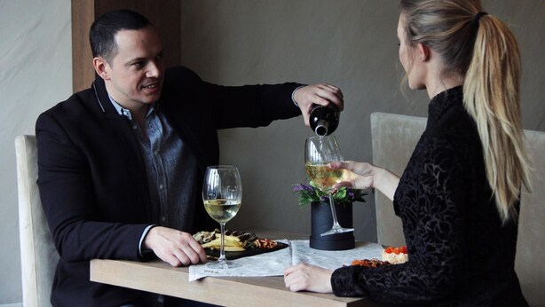 Een eettafel met twee personen, waarvan er één wijn inschenkt.