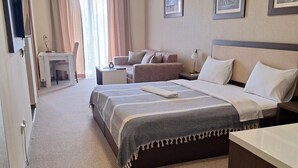 Een hotelkamer met een groot bed, een bureau, een stoel en een sofa. Twee ingelijste foto's hangen aan de muur.