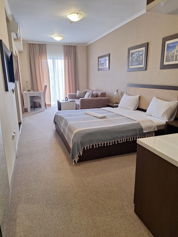 A hotel room with a large bed, a desk, a chair, and a sofa. There are two framed pictures on the wall.